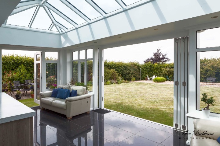 Country Hardwood modern orangery with white timber roof lantern and bi-fold doors, interior view opening onto garden.