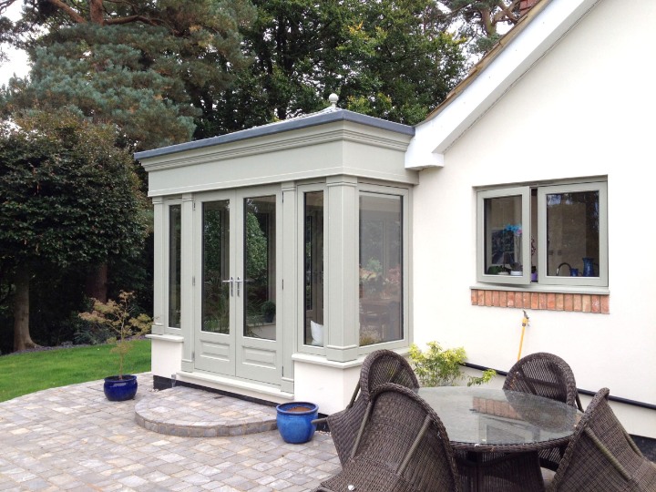 Bespoke Country Hardwood orangery extension with French doors and painted timber frames, opening onto a stone patio with outdoor dining set.
